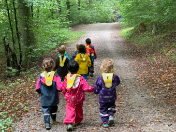 Several children are walking on a path through the forest.